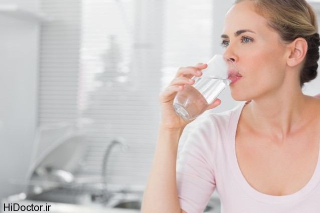 Pensive blond woman drinking water in her kitchen