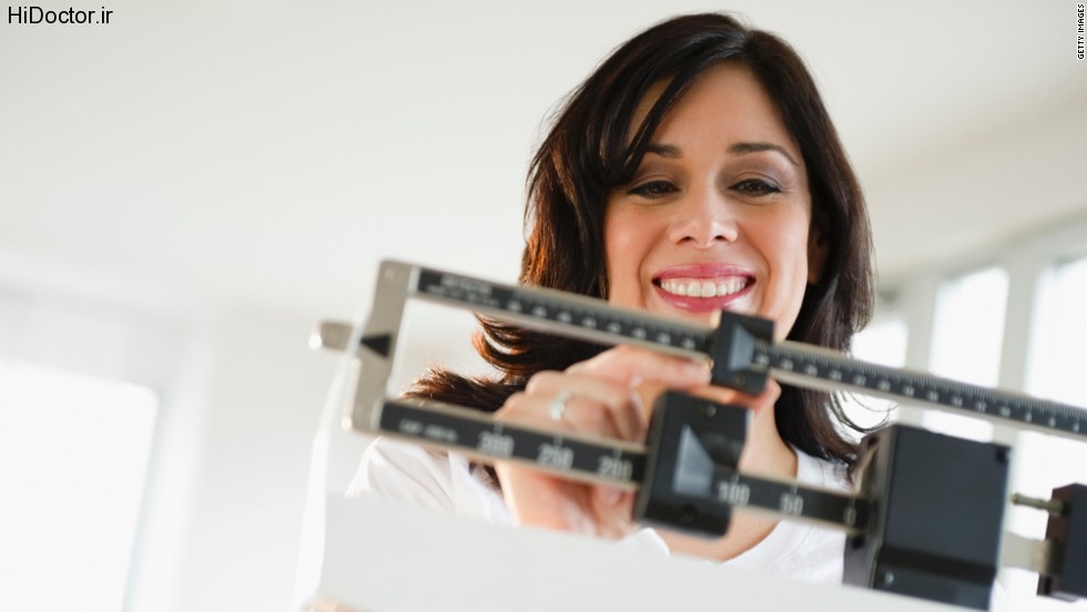 Smiling Hispanic woman weighing herself on scale