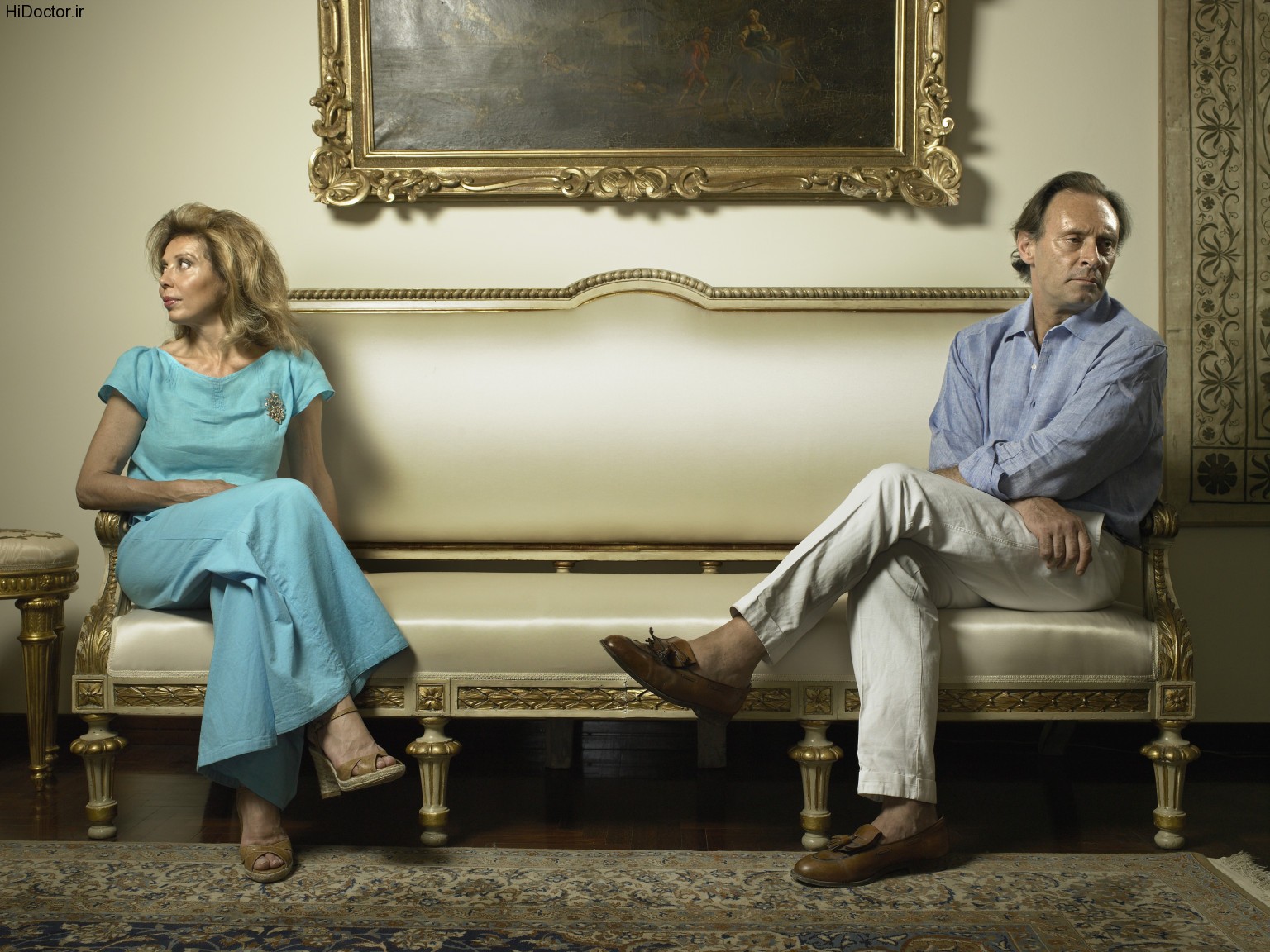 Mature couple sitting at opposite ends of couch, looking away