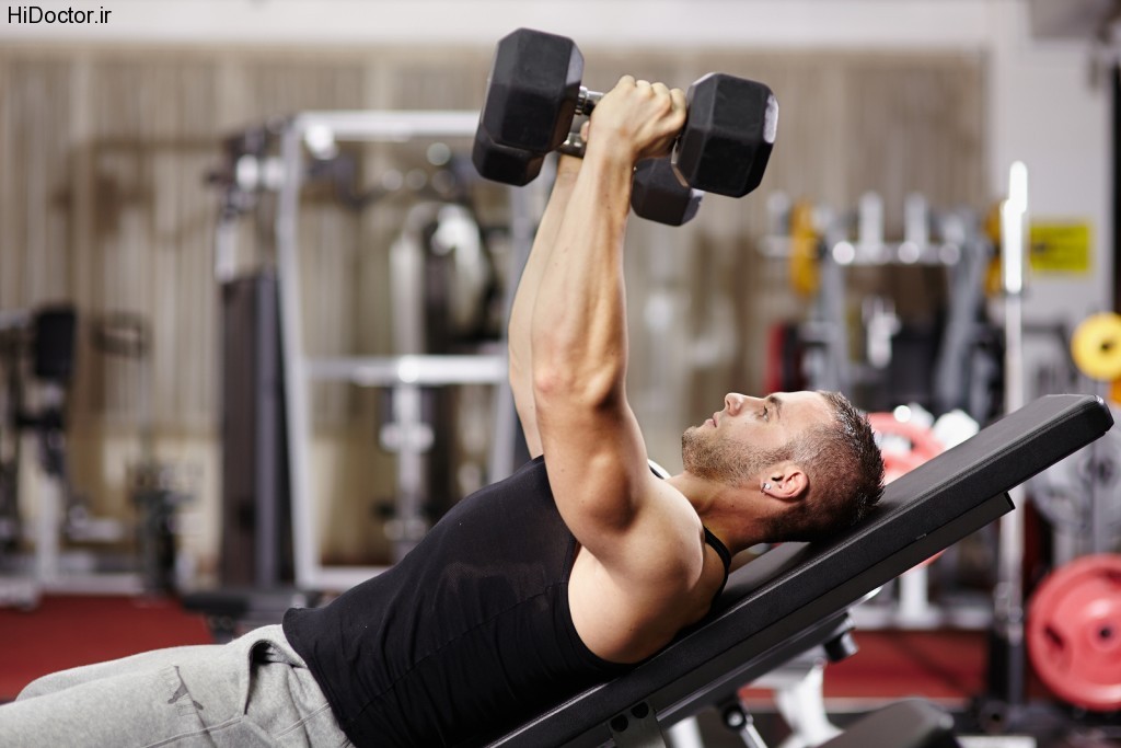 Athletic young man laid on back working his chest with heavy dumbbells