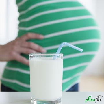 Mid section of pregnant woman, glass of milk in front