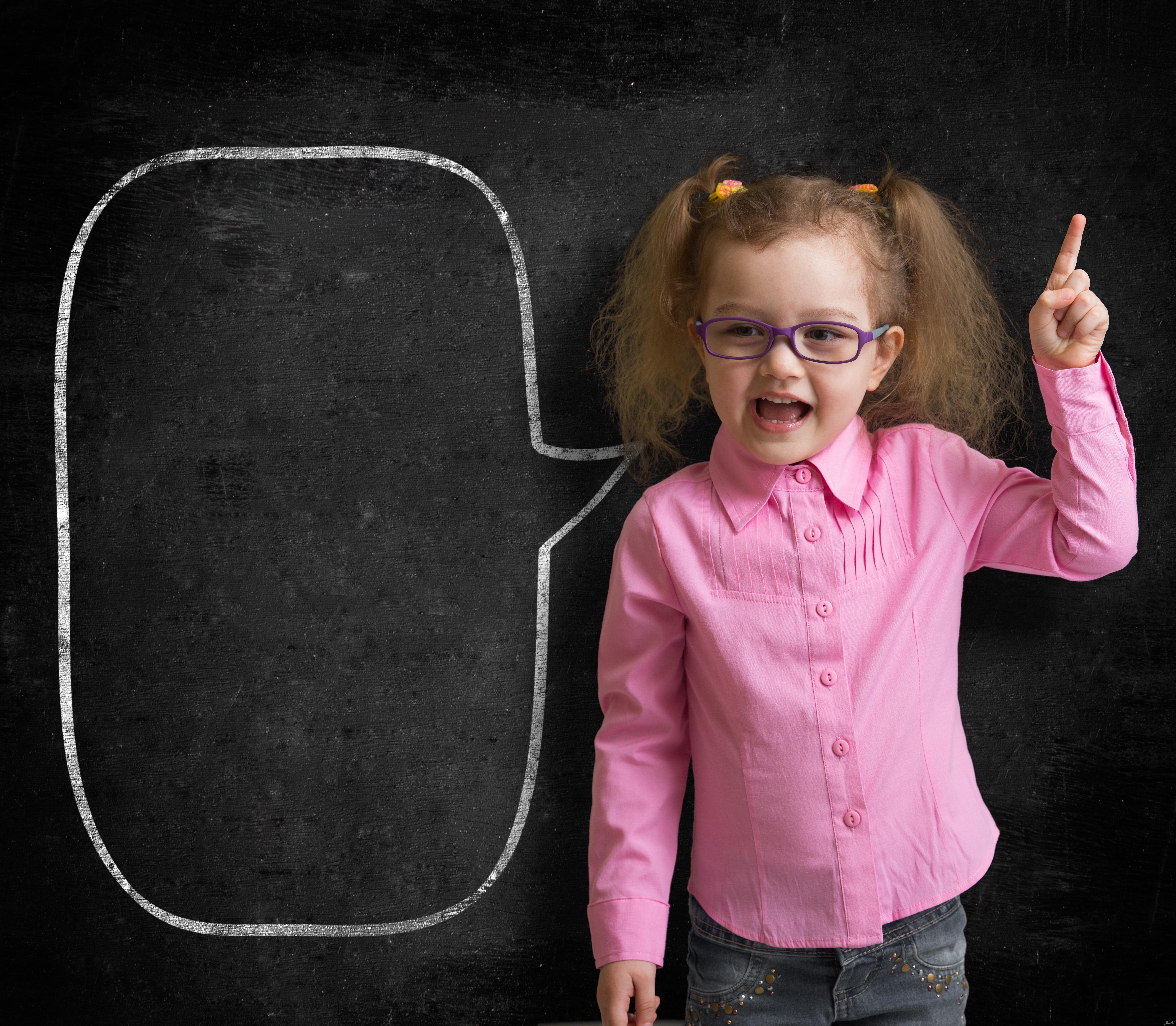 Funny child in eyeglasses standing near school chalkboard as a teacher with blank speech bubble scetch.