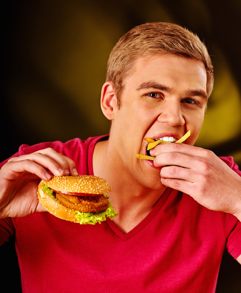 Young man eats greedily big hamburger. Fastfood concept.